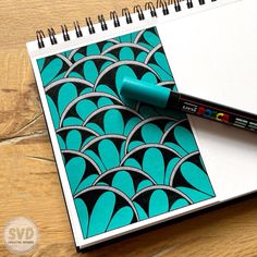 a spiral notebook with a blue and black design on it, next to a marker