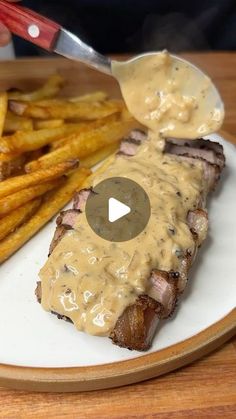 a plate with french fries, steak and gravy on it next to a knife