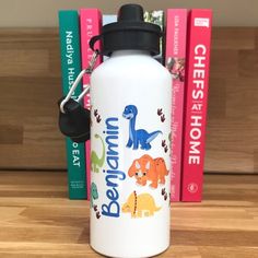 a white water bottle sitting on top of a wooden table next to books and a black keychain