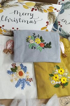 three embroidered christmas gifts are sitting on top of a pile of white and yellow fabric