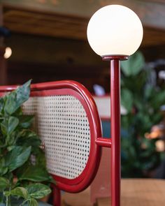 a red table lamp sitting on top of a wooden table next to a potted plant