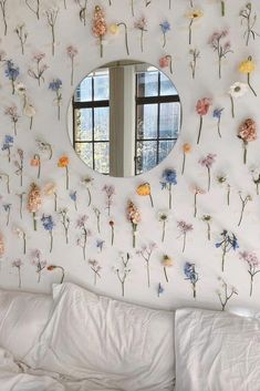 a bedroom with flowers on the wall and a round mirror above it's bed