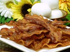 bacon strips on a white plate next to sunflowers and an egg in a basket