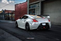 a white nissan sports car parked in front of a brick building with graffiti on it