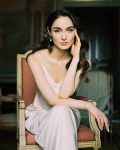 a woman sitting in a chair with her hand on her cheek and looking at the camera