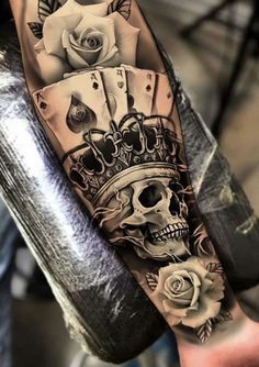 a man's arm with playing cards and roses on it, while he is wearing a