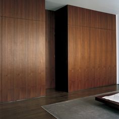 a bed sitting on top of a wooden floor next to a wall covered in wood paneling