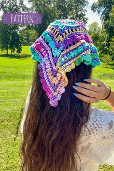 a woman with long brown hair wearing a colorful crochet hat in the park