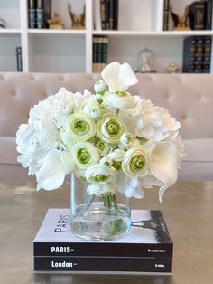 a vase filled with white flowers sitting on top of a table next to a book