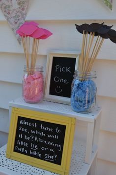 a table topped with jars filled with pink and blue candies next to a chalkboard sign