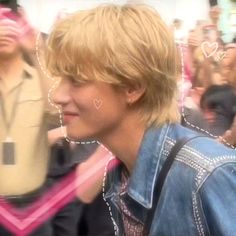 a blurry photo of a man with blonde hair and blue denim jacket in front of a group of people