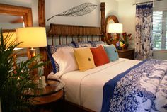 a bedroom with blue and white bedding, wooden headboard, lamps, and plants