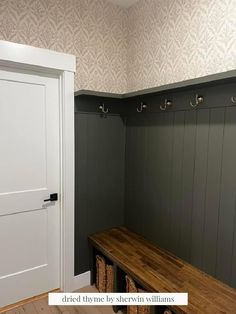 a wooden bench sitting in the middle of a room next to a white door with hooks on it