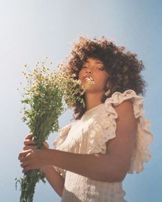 a woman holding flowers in her hands and looking up at the sky with one eye open