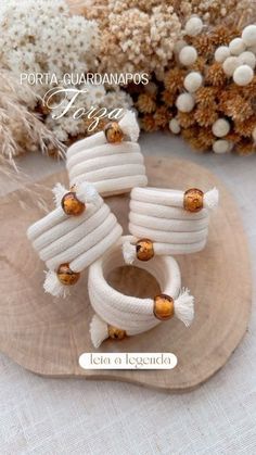 three white bracelets with gold beads on top of a wooden plate next to dried flowers