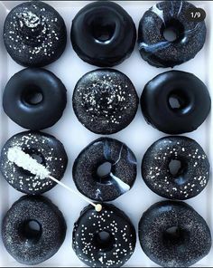 a box filled with black donuts covered in sprinkles and white frosting