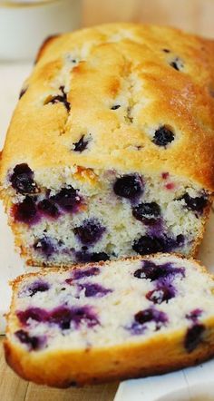 a loaf of blueberry bread sitting on top of a cutting board next to a cup