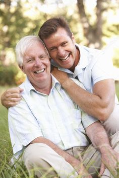 two men sitting in the grass hugging each other and smiling at the camera stock photo