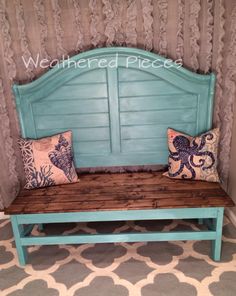 a wooden bench with two pillows on it and a wall hanging behind the headboard