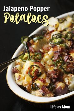 a bowl filled with potatoes and bacon on top of a black table next to a spoon