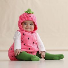 a baby sitting on the floor wearing a pink and green outfit with a strawberry hat