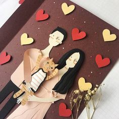 a paper cut out of two people holding a cat on top of a card with hearts