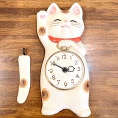 a white cat clock sitting on top of a wooden table next to a knife and fork