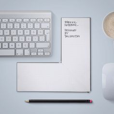 a computer keyboard, mouse and notepad on a desk with a cup of coffee