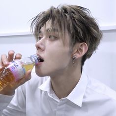 a young man drinking from a bottle while sitting in front of a white wall with his eyes closed