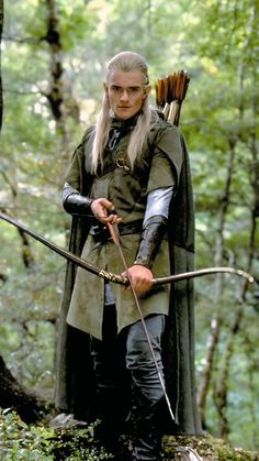 a man dressed in medieval clothing holding a bow and arrow while standing in the woods