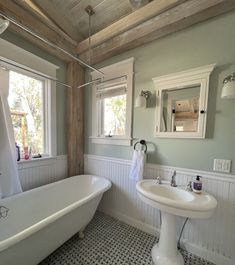 a white bath tub sitting next to a sink in a bathroom under two windows with wooden beams