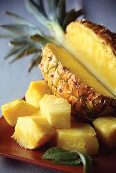 a pineapple and sliced pineapple on a red plate with minty garnish