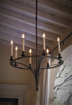 a chandelier with six lit candles hanging from it's center beam in a room