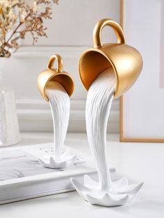 two white and gold vases sitting on top of a table next to a book