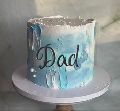 a blue and white cake with the word dad on it sitting on a plate in front of a marble background