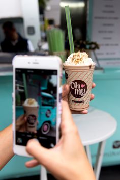 a person holding up a cell phone to take a picture of an ice cream sundae