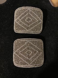 two silver beaded coasters sitting on top of a black table