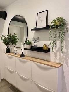 there is a mirror and some plants on the shelf in this room with white walls