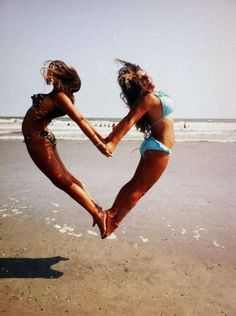 two girls are playing in the sand at the beach with their arms around each other