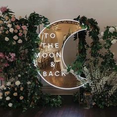 the moon and back sign is lit up with flowers in front of it, along with greenery