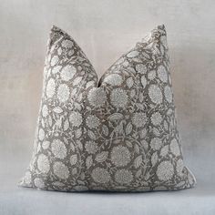 a gray and white floral pillow sitting on top of a table