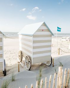 there is a small beach hut on wheels in the sand near some grass and fence