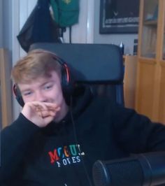 a young man wearing headphones while sitting in front of a computer monitor and holding his hand to his mouth