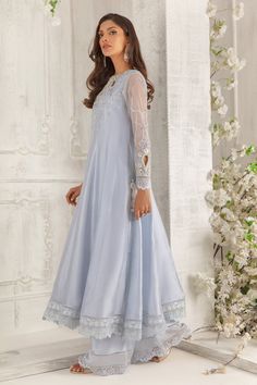 Graceful, feminine and modern, this impeccably tailored flowy kalidar is intricately hand embellished with 3D blooms, subtly shimmering translucent sequins, pearls, Swarovski crystals, offset with hints of lavender in stylish cut work neckline. Flattering net sleeves delicately embellished to uplift the entire outfit. This paneled silhouette is finished with eye-let embroidered border and lace, paired with wide- legged matching pants. Embroidered net two-toned dupatta with delicate crystals, seq Raw Silk Dress, Net Sleeves, Designer Outfit, Embroidered Border, Simple Pakistani Dresses, Pakistani Designers, Designs For Dresses, Matching Pants, Cut Work