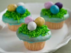 three cupcakes decorated with green grass and small eggs on top, sitting on a plate