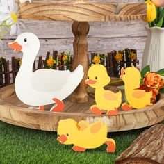 some paper ducks are sitting in the grass near flowers and a wooden stand with yellow ducklings on it