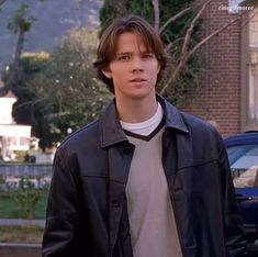 a young man standing in front of a building wearing a black jacket and white shirt