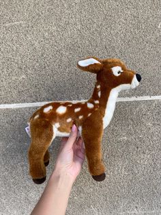 a hand holding a small stuffed deer on the ground