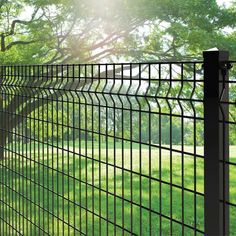 a black metal fence in the middle of a grassy area with trees and grass behind it