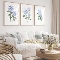 a living room filled with white furniture and paintings on the wall above it's coffee table